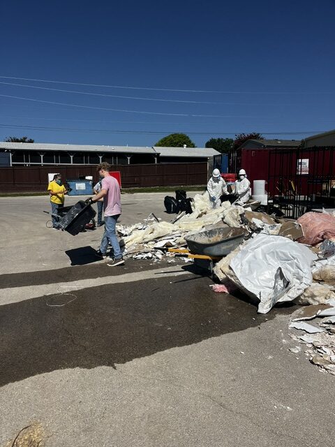 Volunteers wearing protective gear, other clothing and yellow shirts work together to clear out debris from inside of buildings.