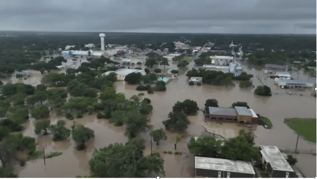 Image shows devastating flooding in Uvalde, Texas. Homes and businesses are submerged under water.