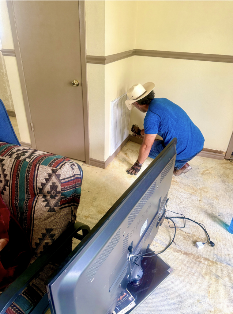 A volunteer uses a tool to remove flood damaged baseboards from a home. 