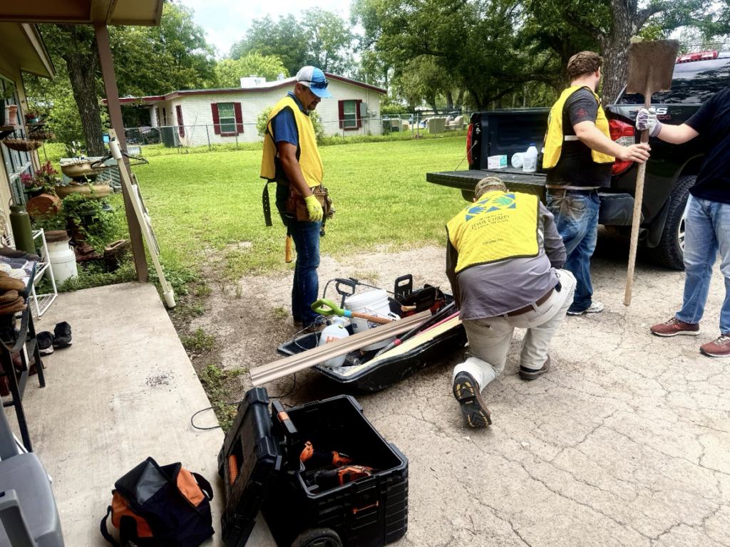 Volunteers holding tools and organize tools. A black truck is seen where volunteers are unloading tools and equipment. The volunteers are wearing yellow vests.